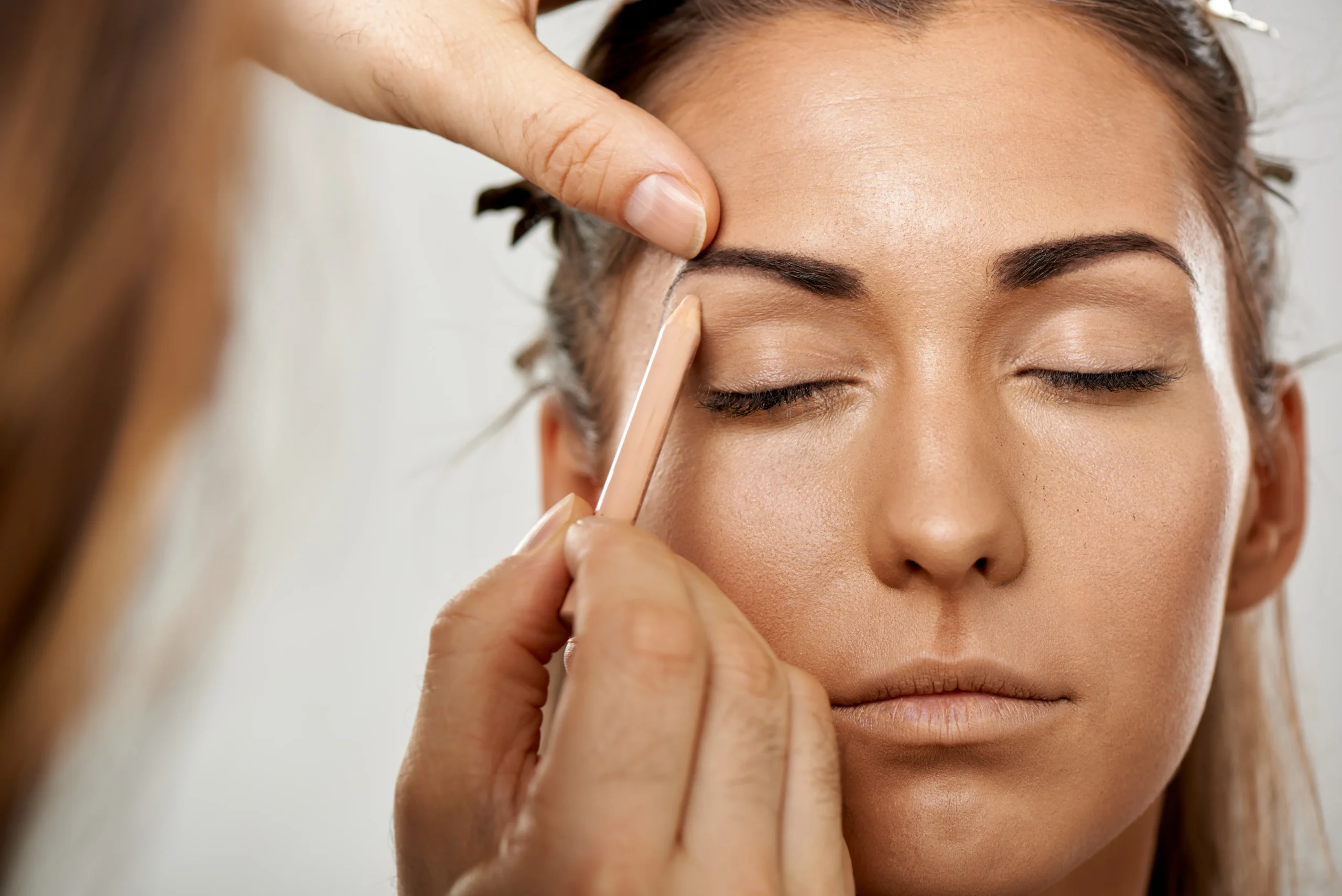 A close-up view of a makeup artist skillfully applying an eyebrow pencil to a woman's face.