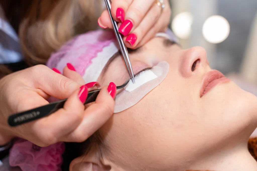 Eyelash extension master with tweezers in his hands performs eyelash correction close-up.