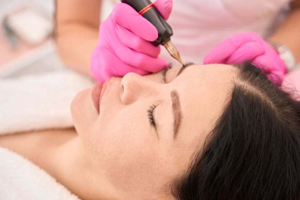 Woman in pink gloves makes a tattoo of eyebrows